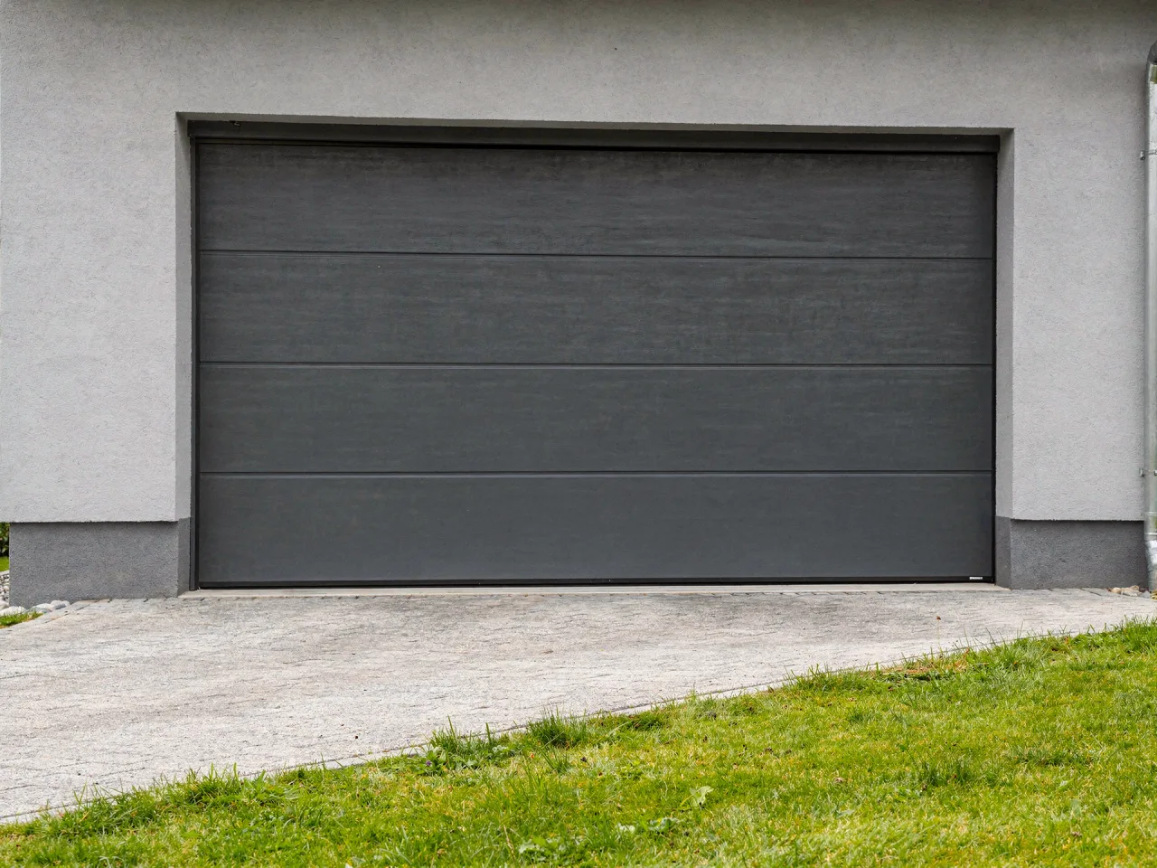 Closed anthracite grey sectional garage door in the facade of a house, with a clean concrete driveway in front