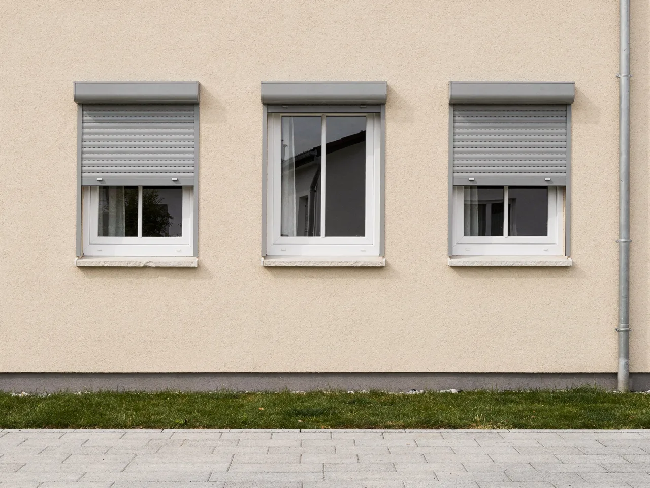 Surface-mounted roller shutters above white windows on a house facade, two of them half lowered